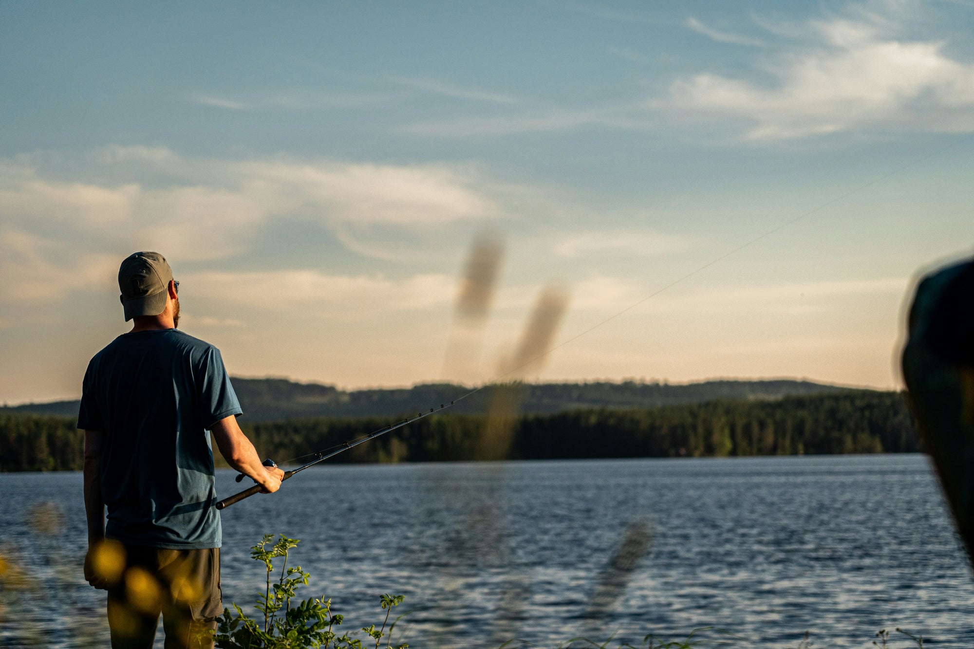 Man in blue t-shirt holding fishing rod near pond